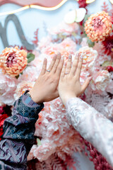 Couple's hands with wedding rings in front of beautiful floral background