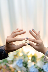 Couple's hands holding wedding rings with sparkling nails and flowers