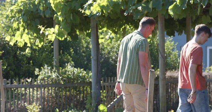 Teenage and adult males walking yard path under pergola adult placing guiding hand teenager leading