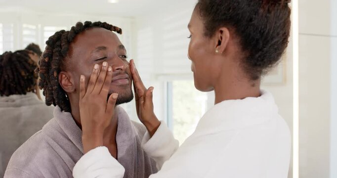 African American couple in bathrobes, woman placing hands, massaging man's face for skincare