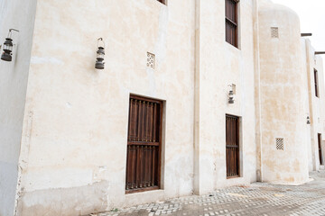 Fototapeta premium Old house wall in Sharjah with vintage kerosene lantern and wooden lattice shutters. Traditional architectural detail reflecting Emirati heritage and Middle Eastern design.
