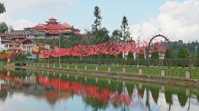 A scenic view of Sapa Lake in Vietnam, showcasing the vibrant red flags adorning the trees along the waterfront, reflecting in the calm water, with a temple in the background.