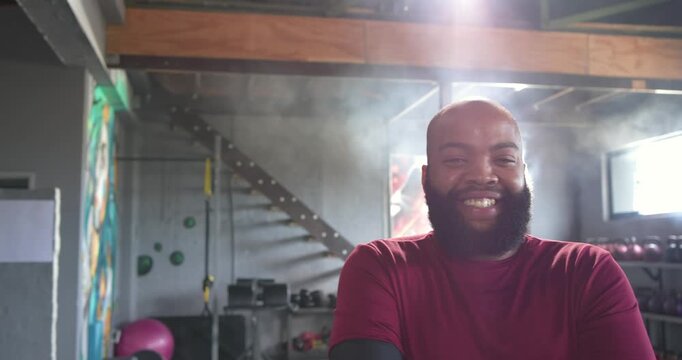 Camera moving closer, man wearing maroon top and black sleeve reacting with laugh among gym weights