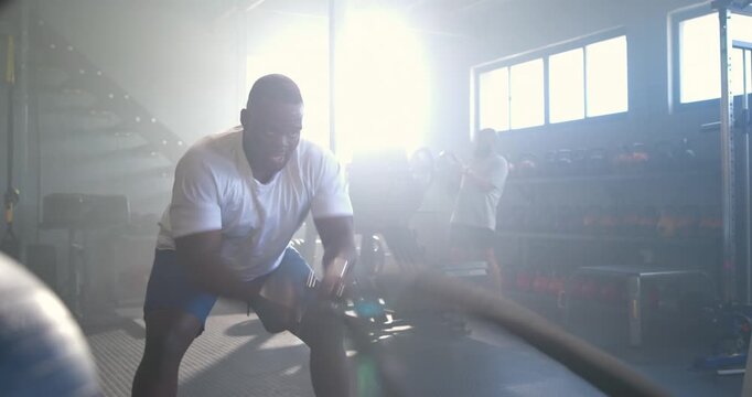 Male partners frontman in shorts gripping anchored ropes making waves at gym for power, copy space