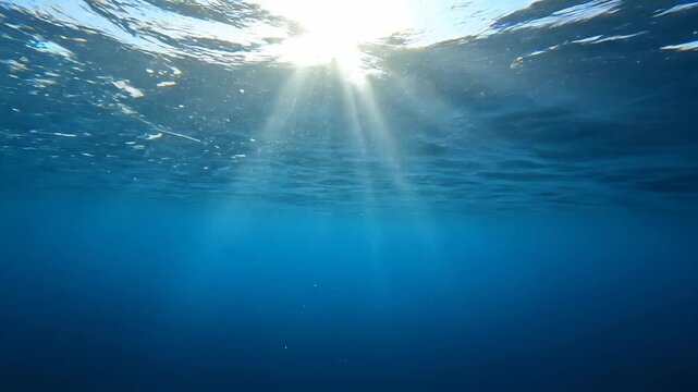 Underwater view of sunlight rays penetrating the clear blue ocean water, with air bubbles ascending towards the surface.