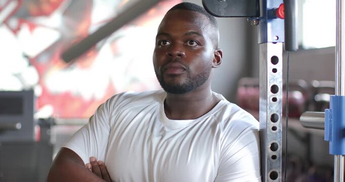Hearing off-camera voice, African American adult man leaning in gym by squat rack, shifting gaze