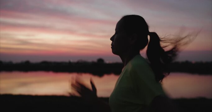 Silhouette Side Profile of Asian Woman Jogging and Running by Lakeside at Golden Hour for Wellness Journey and Self Care, 	 Tracking shot    