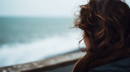 Woman with brown hair is looking out at the ocean