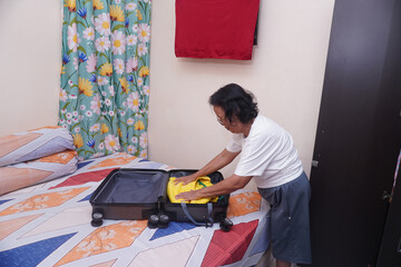 Fototapeta premium Senior woman folding yellow clothes into suitcase