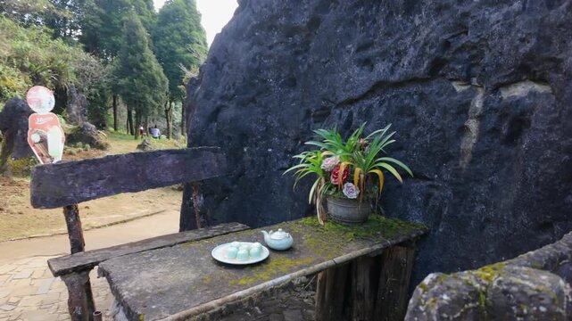 A serene rest stop in Ham Rong Park, Sapa, L&agrave;o Cai, Vietnam.. A stone table with tea set and flowers offers respite amidst lush greenery and towering rock formations.