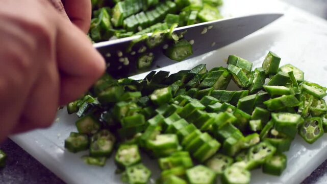 Chopping fresh okra into small pieces on cutting board preparing for cooking healthy meal