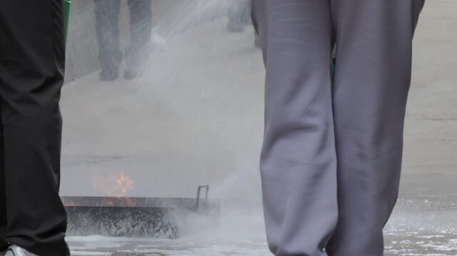 Fire extinguisher training safety drill, emergency response workplace session, trainee outdoor green unit, instructor foam spray, dry powder officer