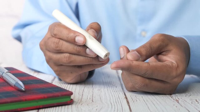 Person performing blood glucose test with lancet device and blood drop