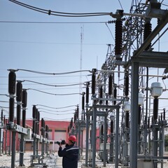 Electrical engineer worker wearing red safety helmet using thermal imaging camera to scan high voltage power substation equipment for predictive maintenance inspection.