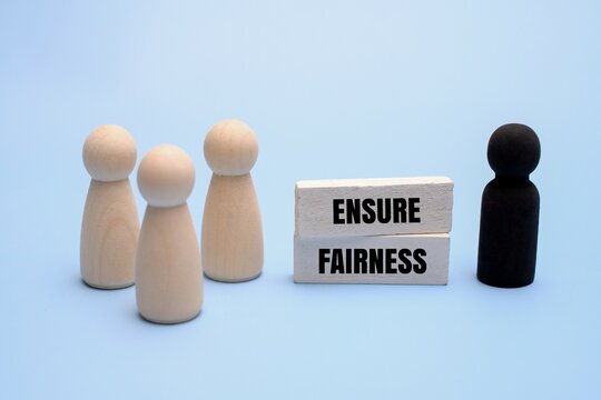 Equality, diversity and the need to overcome racial or color bias in society and business concept with text ENSURE FAIRNESS next to wooden figurines