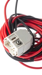 Close-up of coiled electrical wiring, featuring red and black insulated cables connected to a white rectangular connector