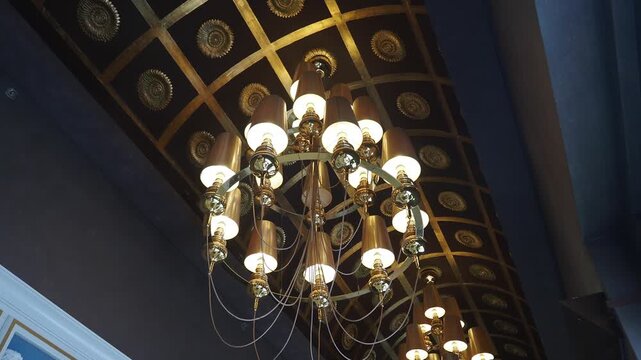 Low angle view of ornate golden chandelier hanging from decorated coffered ceiling in luxurious interior