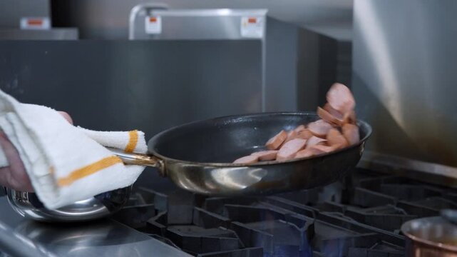 Chef searing meat in a pan on a professional gas stove in a commercial kitchen