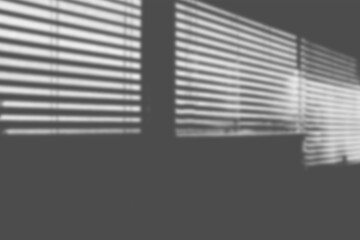Naklejka premium Horizontal blinds sunlight shadow overlay stretching across dark room wall creating cinematic moody lines for modern interior photography