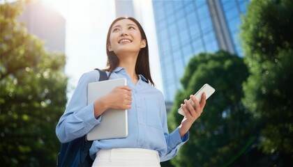 オフィス街でノートパソコンとスマートフォンを持ち見上げる女性
