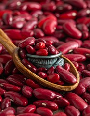 Close-up of glossy, deep-red kidney beans filling a wooden spoon and surrounding the spoon's contents. Rich colours and texture