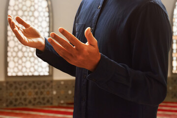 Hands of young asian muslim man praying in the mosque window arch, eid adha mubarak concept