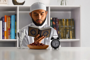 Young asian muslim man with beard reading holy book quran at home, eid adha mubarak concept