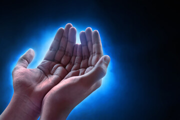 Hands of young asian muslim man praying on dark blue background, eid adha mubarak concept