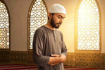 Portrait of young asian muslim man with beard praying in the mosque window arch, eid adha mubarak concept