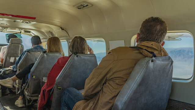 People are sitting in a row in the cabin of a small plane, looking out the windows. View from the back. The captain is ahead. Peru. Flying over the Nazca Plateau