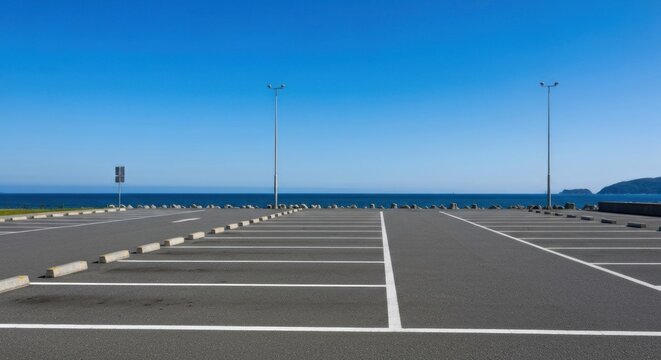 Empty seaside parking lot under a bright blue sky, facing a calm ocean view