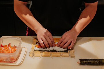 Chef's hand rolling up sushi on a bamboo mat. © Anastasia