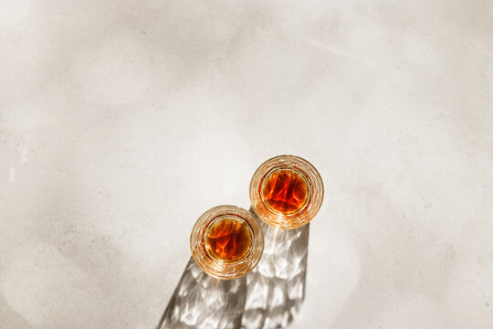 Crystal Whiskey Glasses with shadows at sunlight on beige concrete background, minimal aesthetic top view shiny glasses, sun glare, stong alcohol drink concept, summer still life top view, copy space