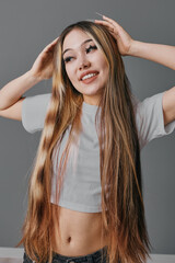 Young woman with long straight hair posing and smiling in casual outfit against neutral background. Fashion, beauty, lifestyle and confident girl with natural makeup and relaxed mood.