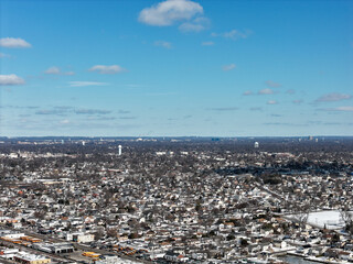 Obraz premium Aerial view of oceanside, new york suburban neighborhood blanketed in winter snow under a bright blue sky, showing rooftops, bare trees and coastal residential sprawl