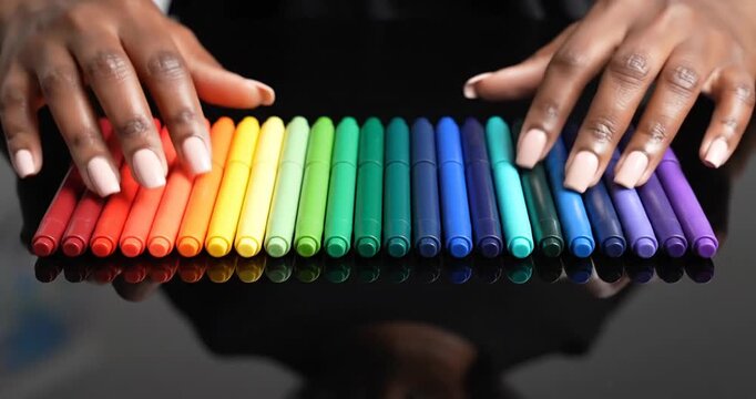 Hands arranging colorful markers on a reflective surface with a blurred background