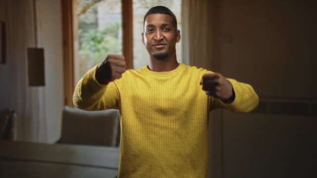 Man in yellow sweater grips imaginary steering wheel with both hands inside a building; confidence composure.