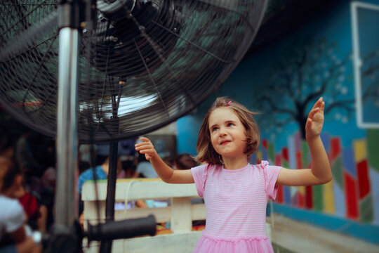 Little Girl Cools Off in Front of an Outdoor Fan in Summer. Young child finds sweet relief from the summer heat in from of an electric fan 