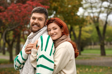 Obraz premium Cute young couple in warm sweaters and scarves hugging at autumn park