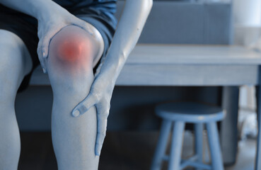 Woman massaging her painful knee with red highlight. Knee osteoarthritis, joint inflammation, patellar tendonitis and injury concept for health care, physical therapy and orthopedic medical treatment.