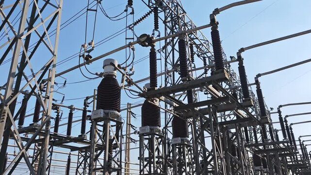 Panning right video view of high voltage electrical power substation switchyard with instrument transformer and disconnect switch equipment on steel structure under blue sky.