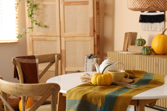 Pumpkin, teapot and cup on table in interior of dining room, closeup