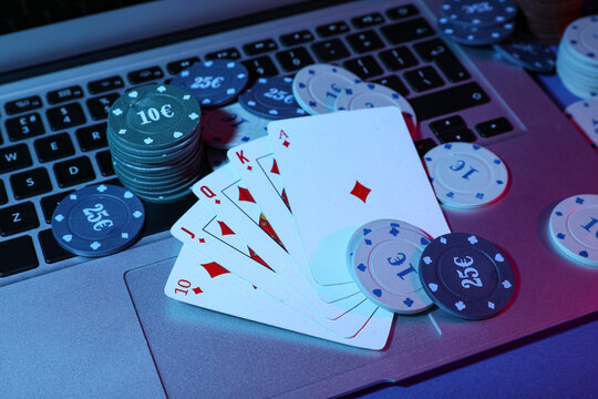 Laptop with playing cards and poker chips on table in casino, closeup