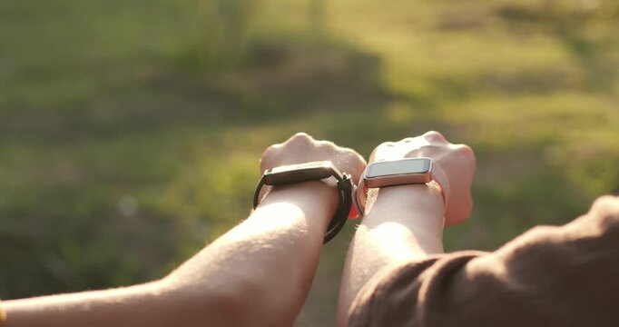 Couple touches wrists wearing smartwatch devices outdoors. Smartwatch technology tracks fitness activity in park. Man woman use smartwatch to share health data sync during sunset walk.
