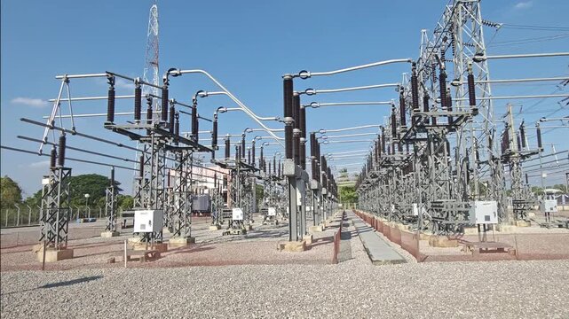 Panning right video view of high voltage electrical power substation switchyard with steel structure and disconnect switch equipment under blue sky for energy grid concept.