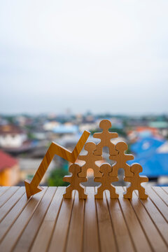 Wooden people figures pyramid with a downward arrow leaning against them on blurred residential background, representing layoffs, downsizing, unemployment, and economic recession concept.