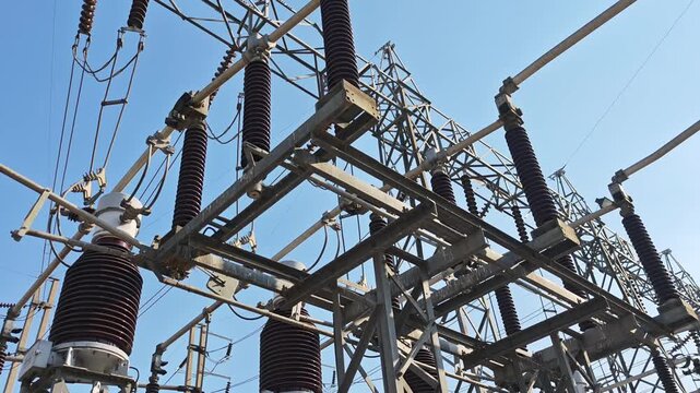 Low angle panning right video view of high voltage electrical power substation switchyard structure with disconnect switch and insulator equipment under blue sky.