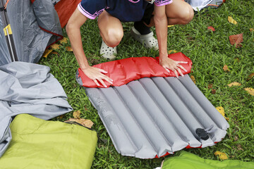 Focused person on grass preparing camping gear for an outdoor adventure, carefully rolling an inflatable red sleeping pad during beautiful autumn day trip © CoreRock