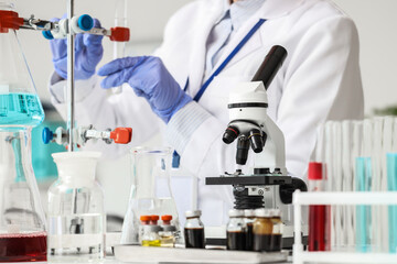 Fototapeta premium Microscope on table against female scientist working in laboratory, closeup