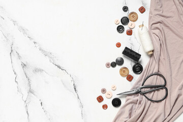 Different colorful buttons with thread spools, scissors and fabric on grunge white background